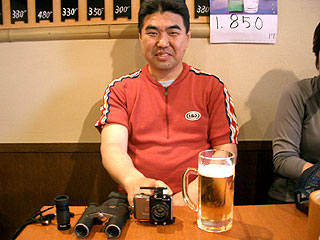 ビール飲みながら単眼鏡、双眼鏡、カメラの説明をするルビオ