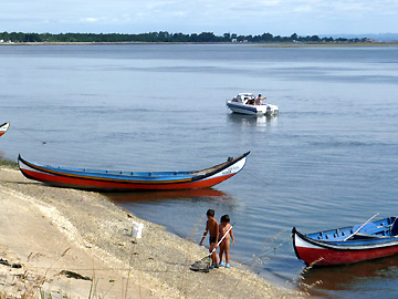 岸辺で遊ぶ子供たちとモータボートで釣りをする大人
